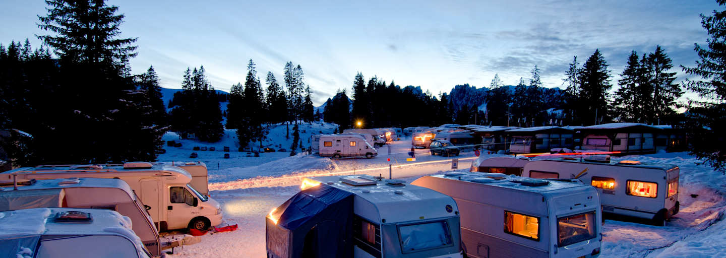 Der Wintercampingplatz Jaunpass bei Nacht. Es liegt Schnee und die Wohnwagen sind hell erleuchtet.