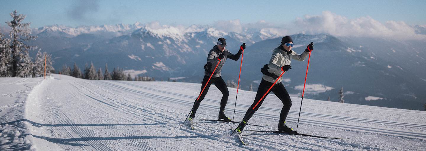Zwei Langläufer auf einer Loipe in der neuen Nordic Kollektion von Löffler.