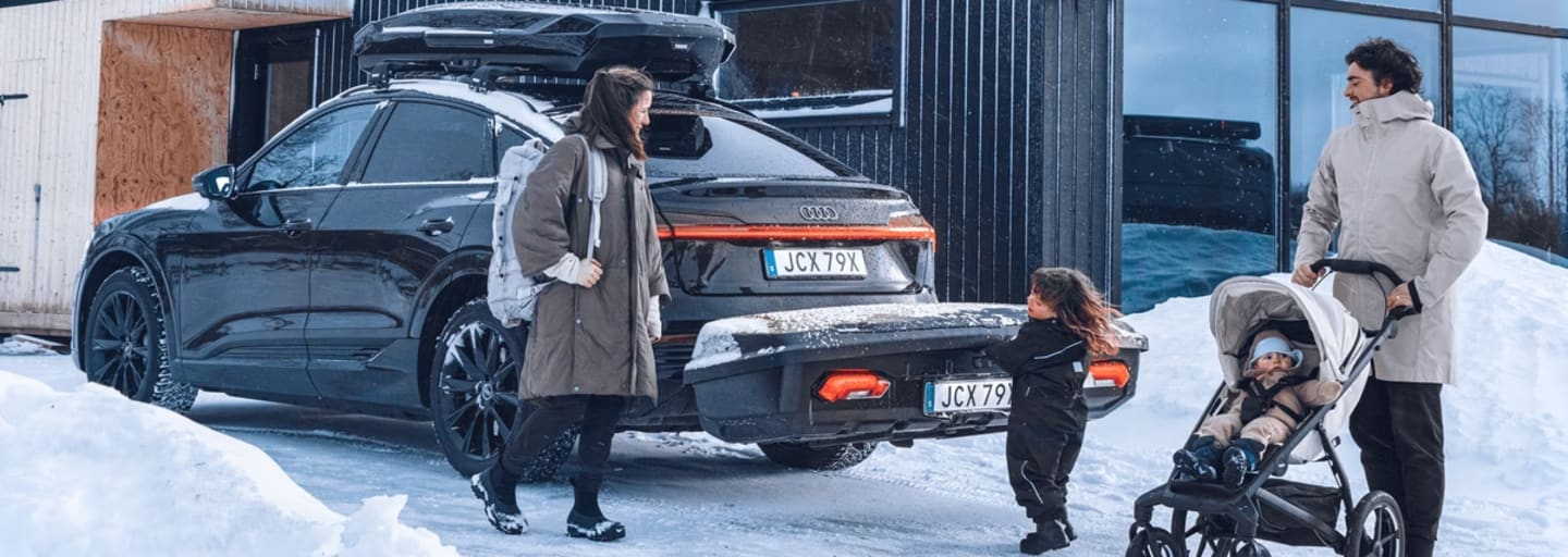 Eine vierköpfige Familie steht vor ihrem Auto, auf dem eine Thule-Heckbox befestigt ist.