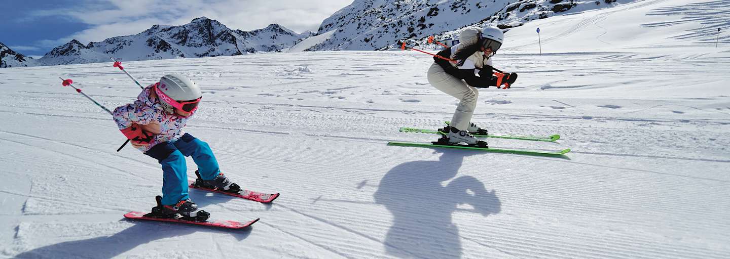 Eine Frau und ein Mädchen fahren gemeinsam Ski und nehmen dabei die Schussposition ein.