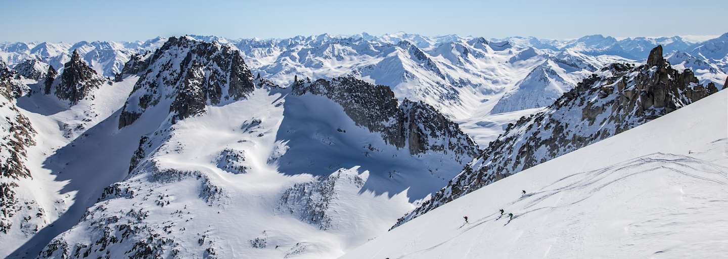 Markante Felsen die vom Schnee bedeckt sind. Skitourengeher fahren einen unverspurten Hang hinunter.