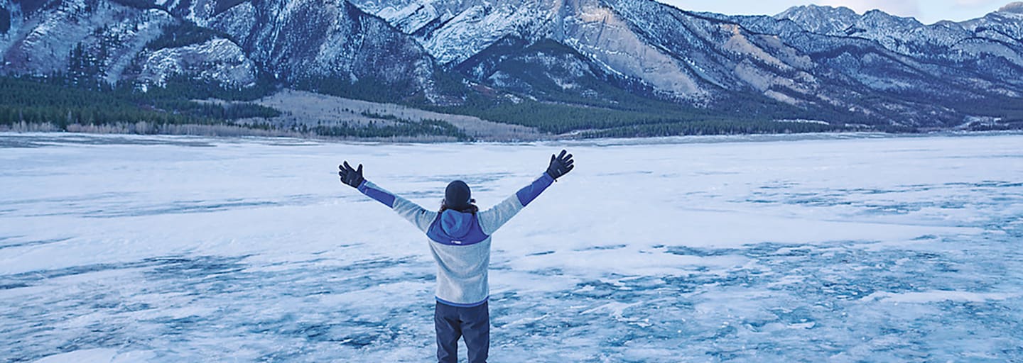 Ein Mann steht vor einem Berg im Schnee mit offenen Armen.