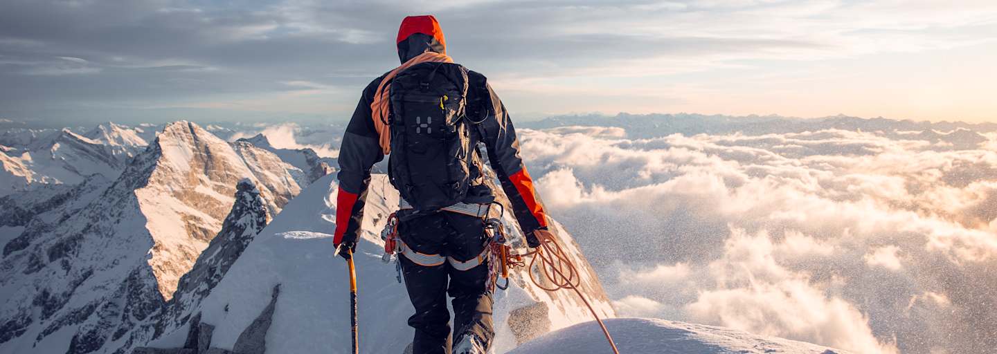 mann beim bergsteigen auf bergspitze, gekleidet in haglöfs