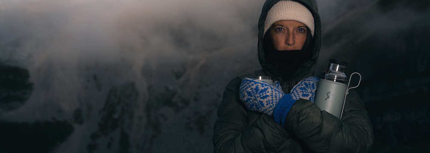 Person in Winterkleidung mit Thermosflasche Hydro Flask Hot Flask & Cup in verschneiter Berglandschaft bei Nebel und eisigen Temperaturen.