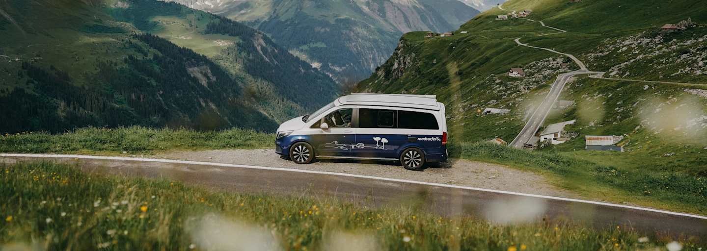 Ein Roadsurfer-Campervan steht am Straßenrand, Blick in die Berge