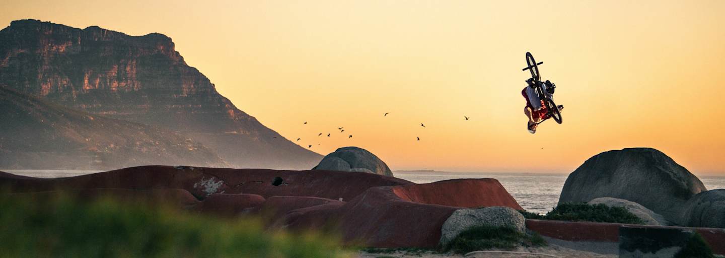 BMX-Biker dreht sich in Luft vor Küstenszenerie.