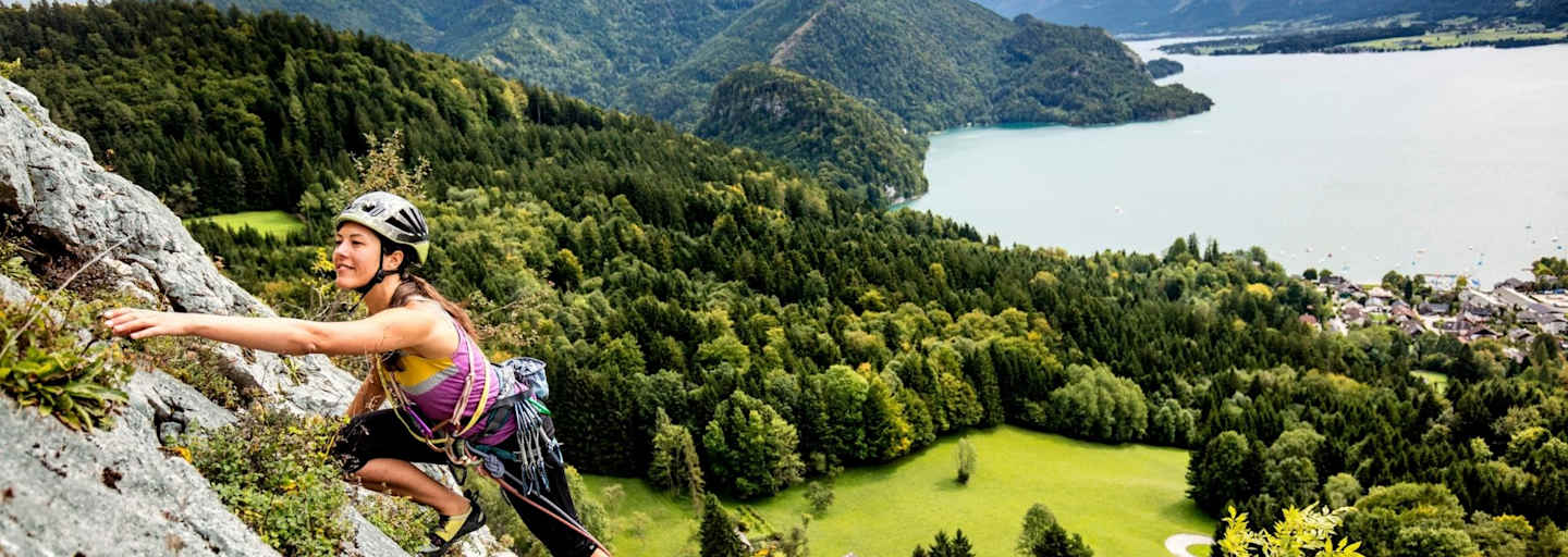 Manuela klettert am Plombergstein, im Hintergrund der türkise Wolfgangsee