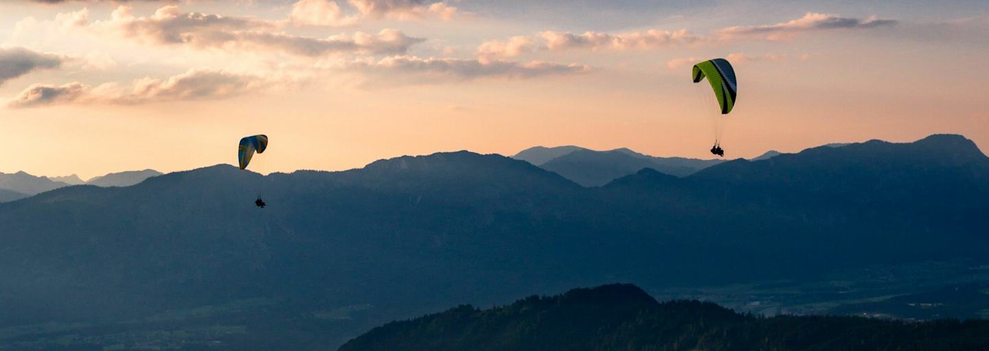 Zwei Personen paragleiten über ein Tal in der Wildschönau.