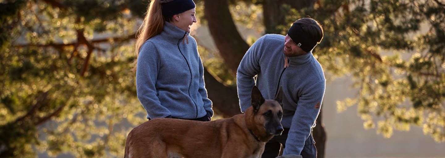 Ein Paar in Sportkleidung aus Merinowolle mit Schäferhund im Park im Herbst.
