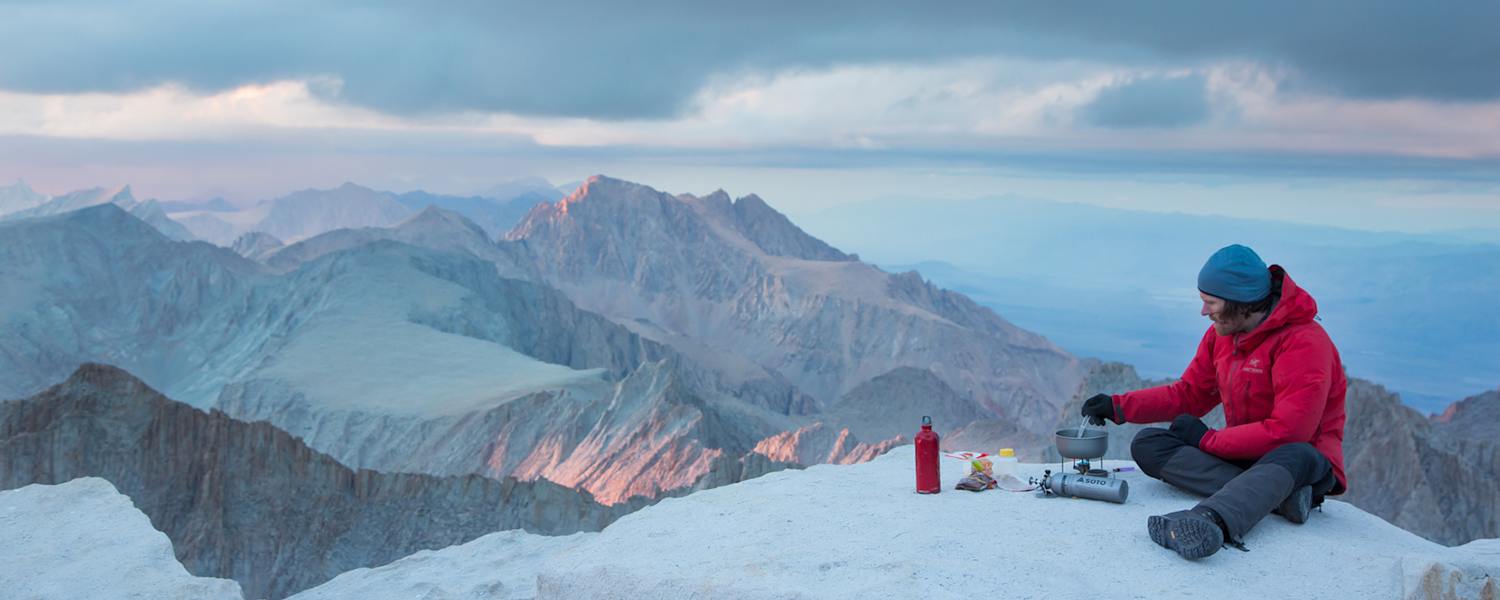 Mann kocht mit SOTO Kocher auf Berg Essen mit Panorama über Berge.