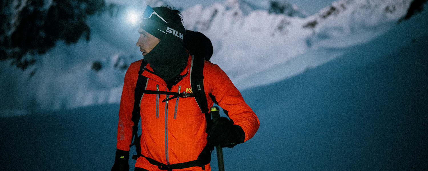 Ein Mann geht im Schnee und Skiausrüstung in der Nacht mit einer Stirnlampe skifahren.