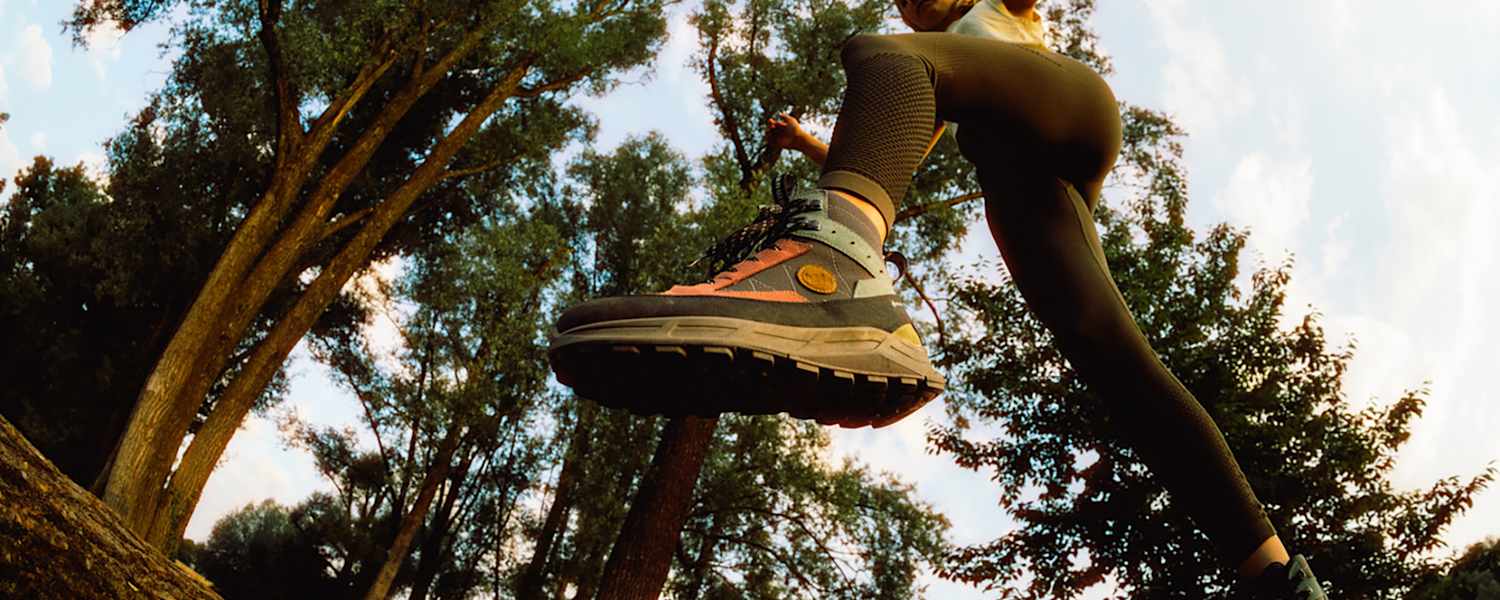 Frau springt im Wald über einen Baumstamm mit dem Hanwag Rotpunkt Light Mid GTX – leichter, vielseitiger Outdoor-Schuh für Alltag und Wanderungen