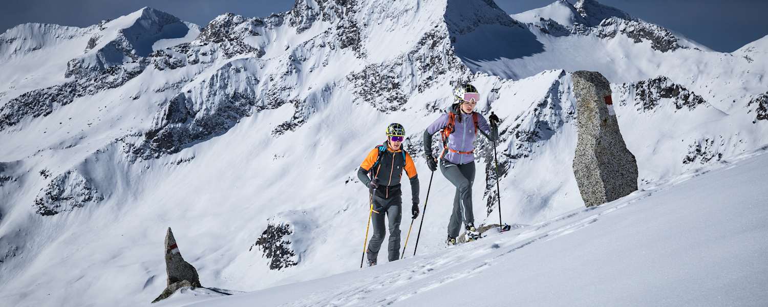 mann und frau beim skitouren gehen auf einem schneebedecktem berggipfel