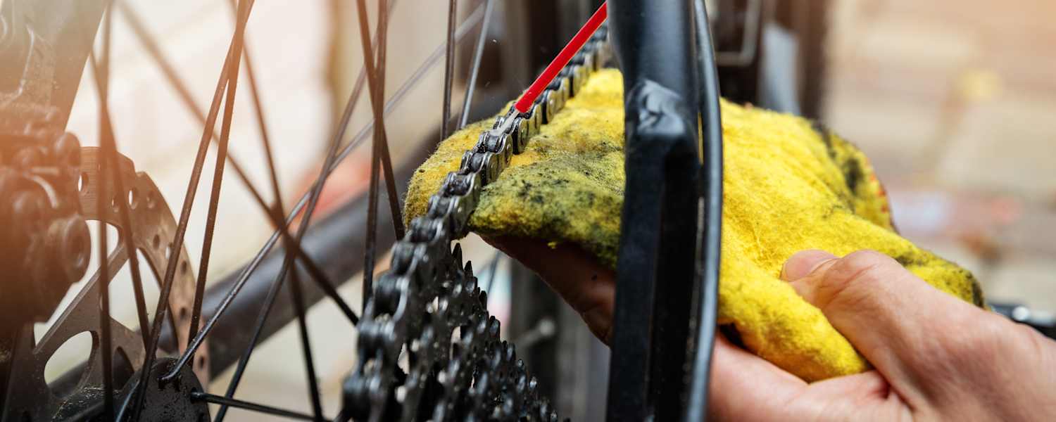 Hand die mit rotem Schlauch und gelbem Lappen eine Fahrradkette schmiert 