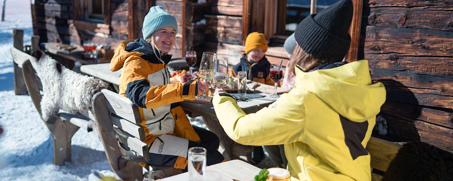 Zwei Damen stoßen mit einem Glas Wein auf der Skihütte im Winter an.
