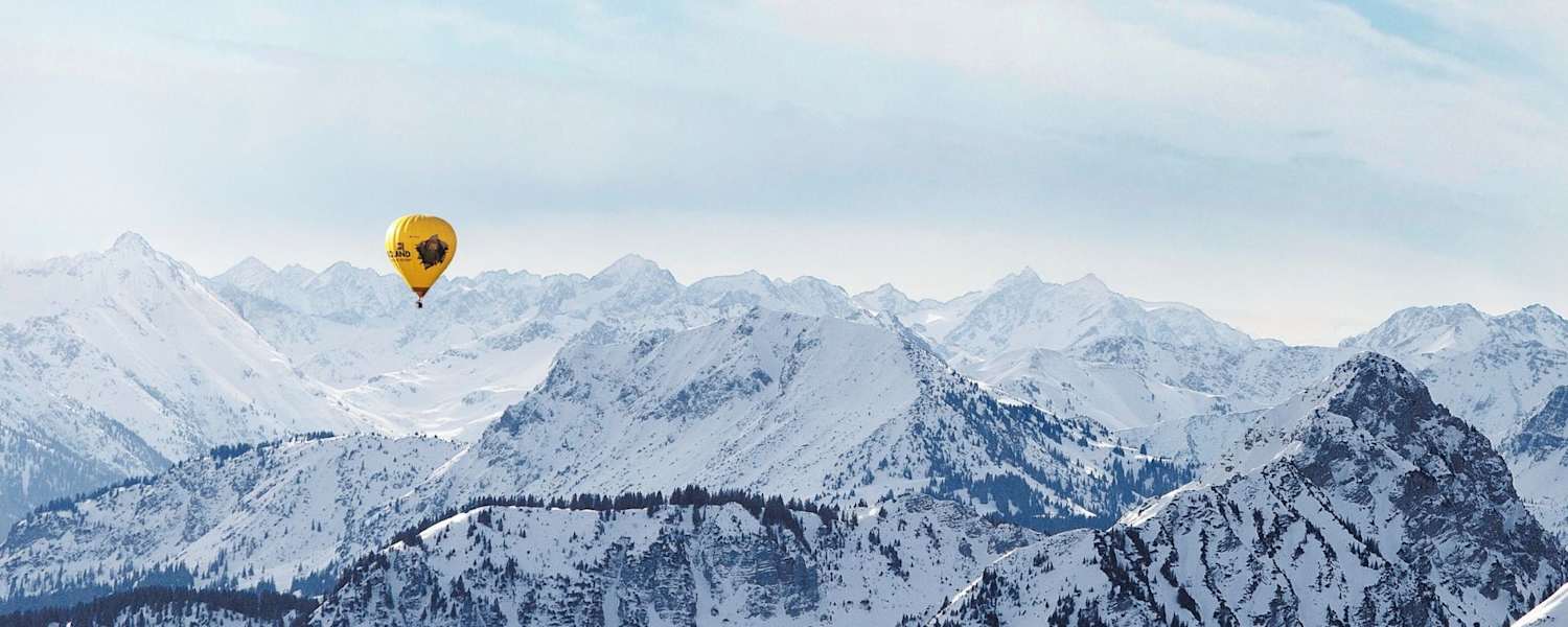 Ein gelber Heißluftballon, dahinter die schneebedeckten Alpen