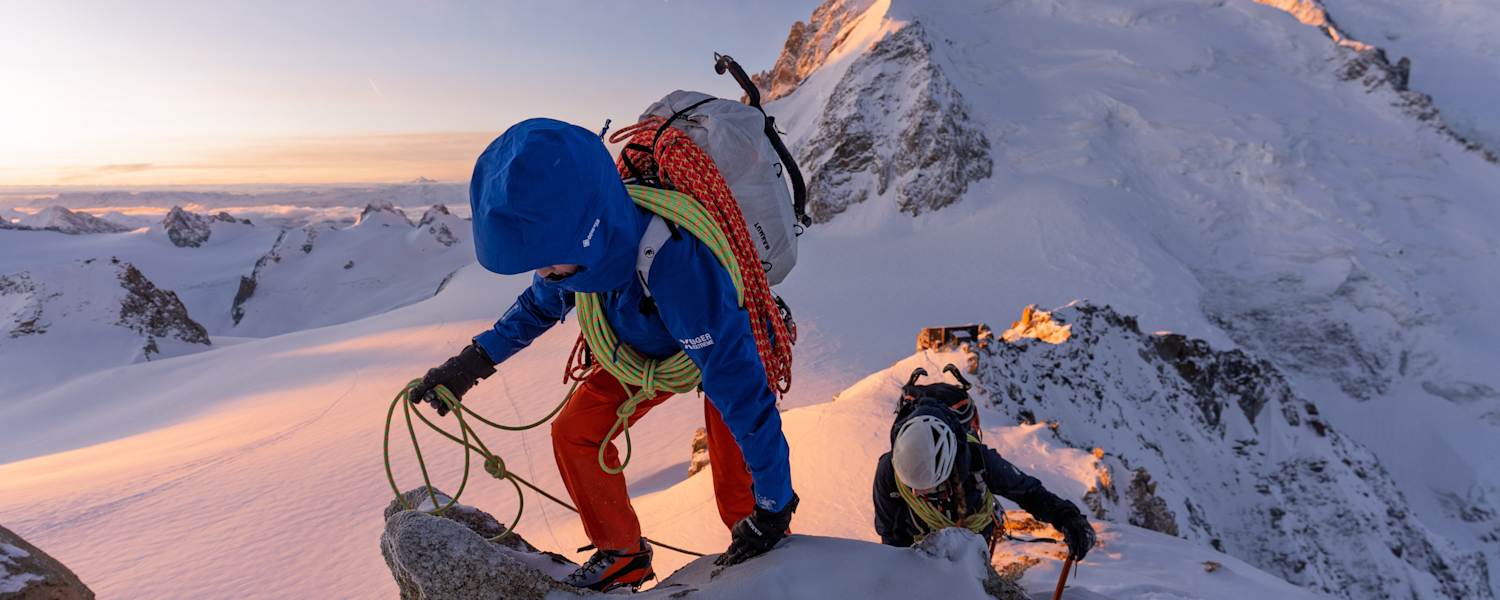 Ein Bergsteiger mit der neuen Mammut Eiger Extreme Kollektion klettert über einen verschneiten Felsgrat. Am kurzen Seil sichert er einen Nachsteiger, der mit einem Eispickel unterwegs ist.