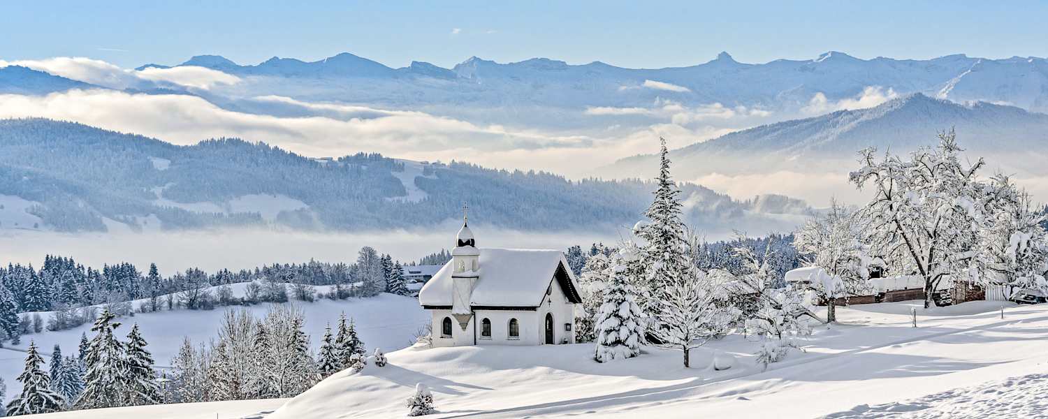 Die Hubertuskapelle in Scheidegg im Allgäu inmitten einer tief verschneiten Berglandschaft.
