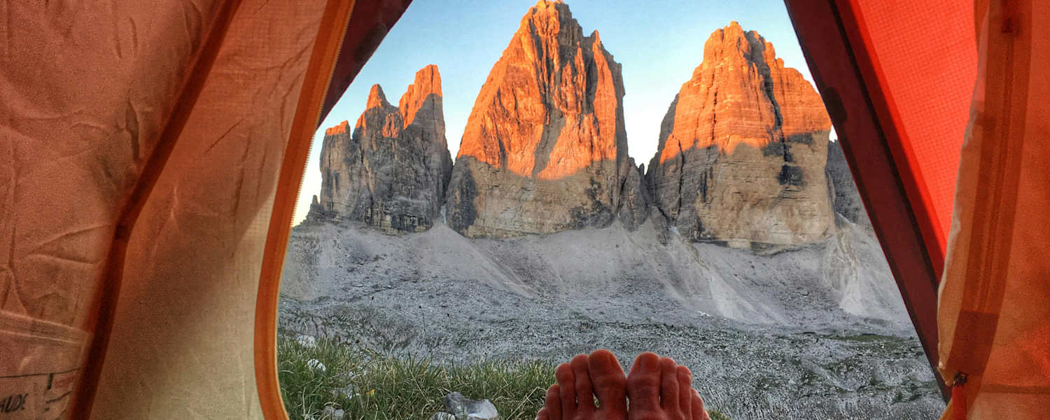 Ein Mann liegt in einem Zelt und genießt den Ausblick auf die Drei Zinnen.