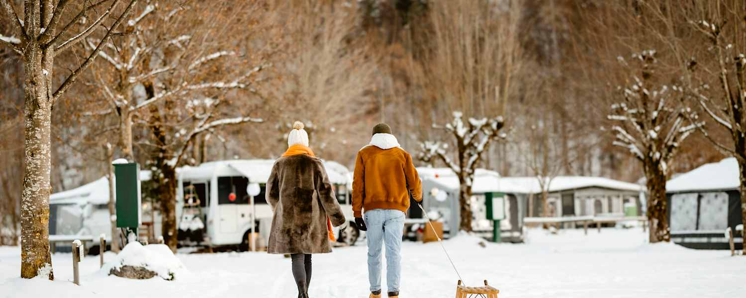Ein Pärchen geht mit einem Rodel über einen Campingplatz im Winter.