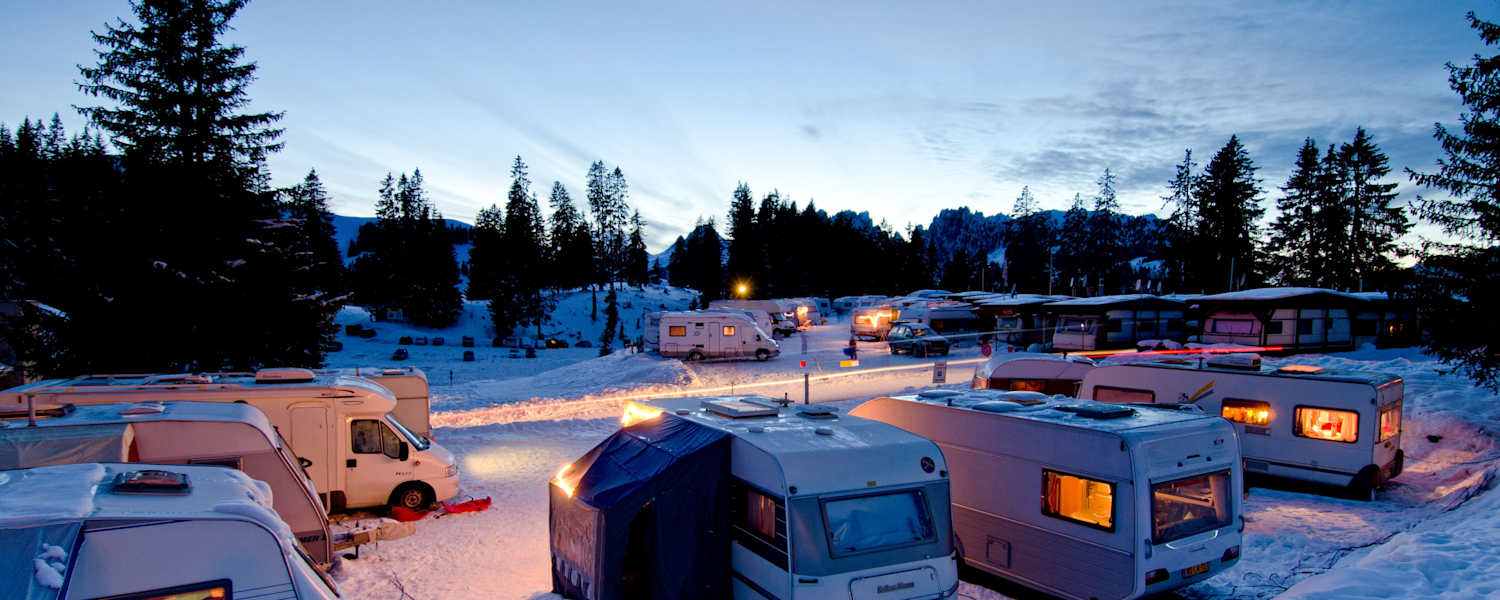 Der Wintercampingplatz Jaunpass bei Nacht. Es liegt Schnee und die Wohnwagen sind hell erleuchtet.