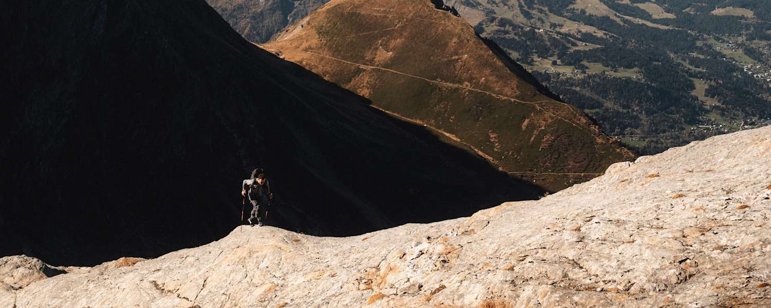 Ein Alpinist steigt einen Berg mit zwei Stöcken und der Haglöfs L.I.M ZT 2.0-Serie hinauf.