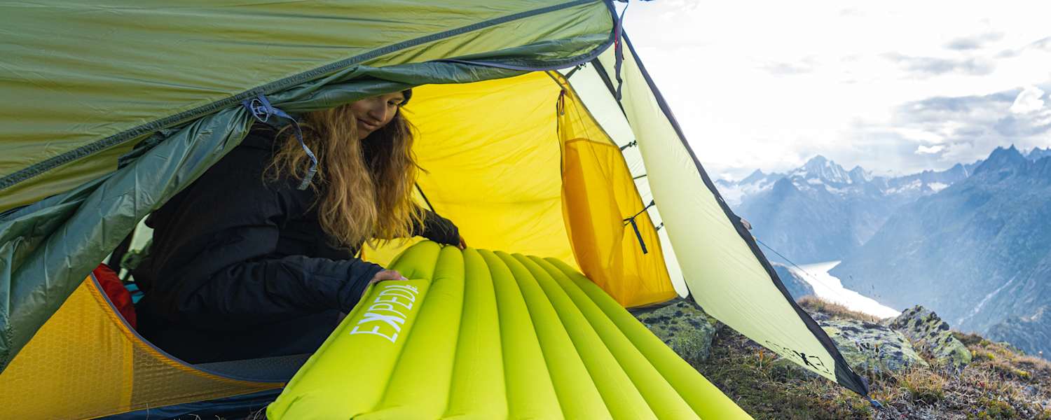 Eine Frau sitzt in einem Zelt und zieht eine Schlafmatte von Exped hinein.