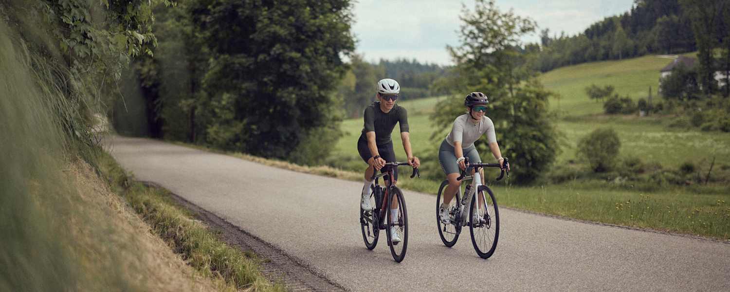 Zwei Radfahrer fahren auf einer ruhigen Landstraße im Mühlviertel bei der Bike Experience, umgeben von grüner Natur und sanften Hügeln.