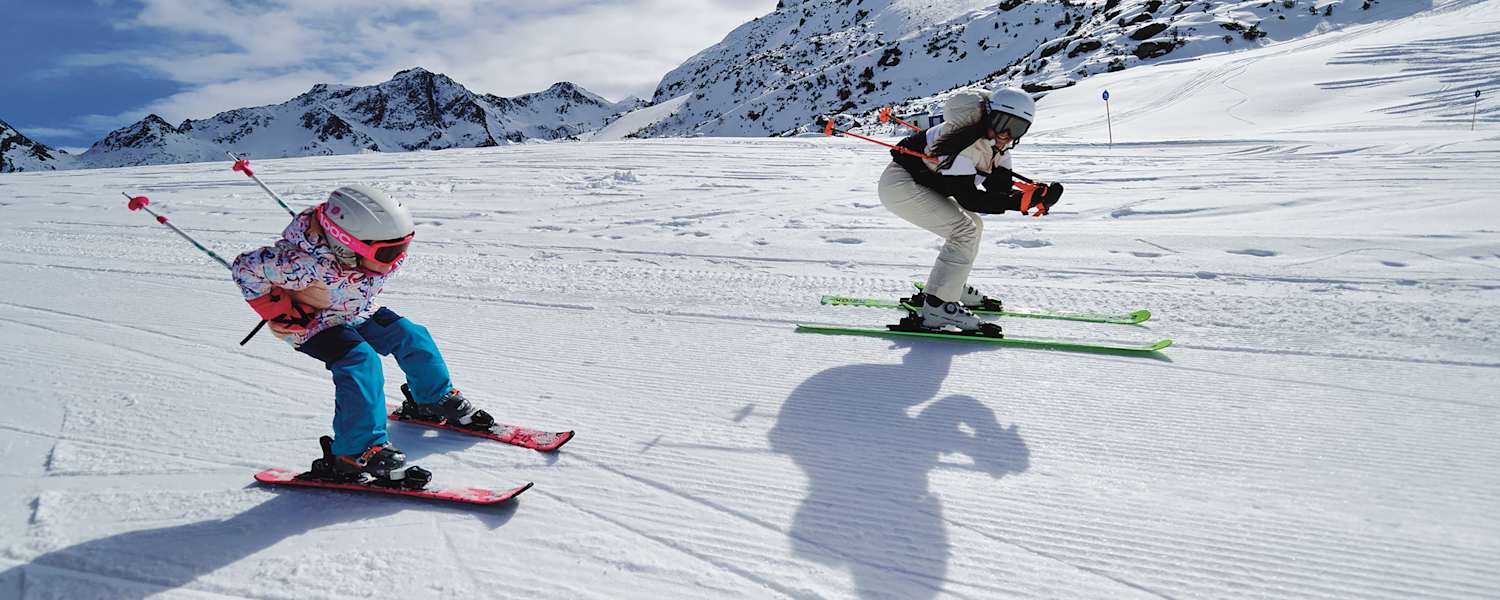 Eine Frau und ein Mädchen fahren gemeinsam Ski und nehmen dabei die Schussposition ein.