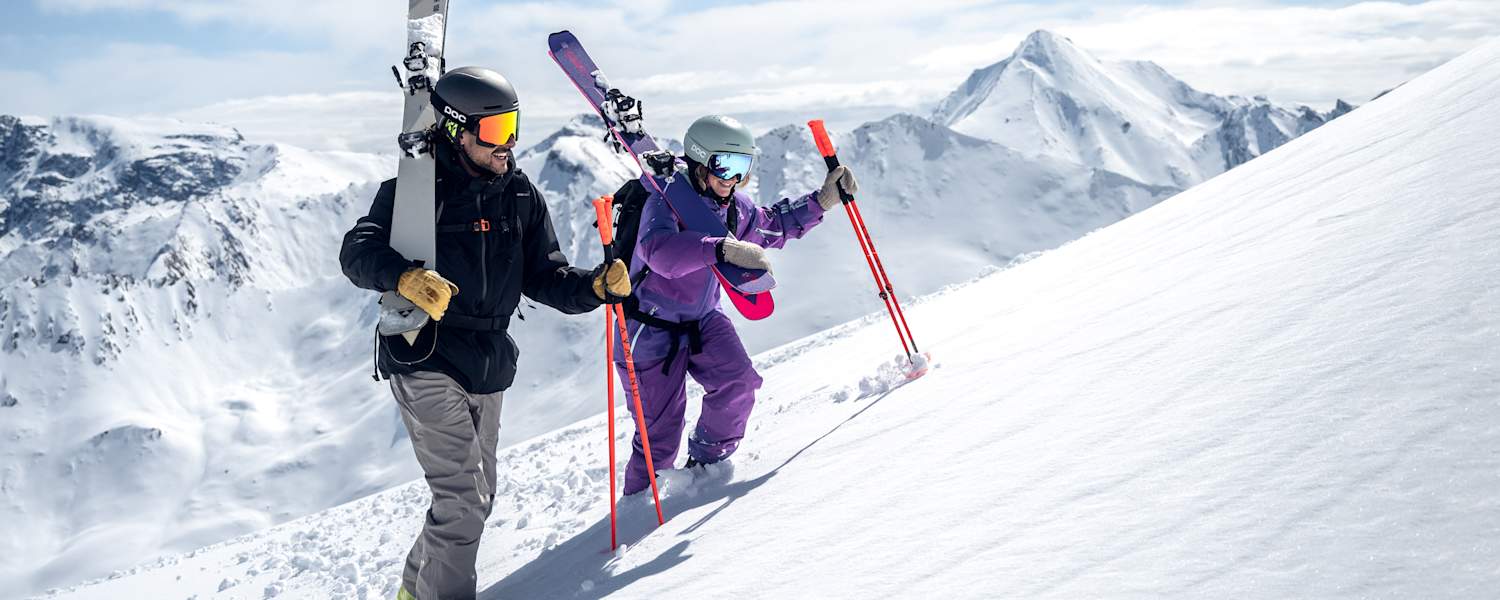 Ein Skifahrer und eine Skifahrerin gehen eine Piste in Ischgl hinauf.