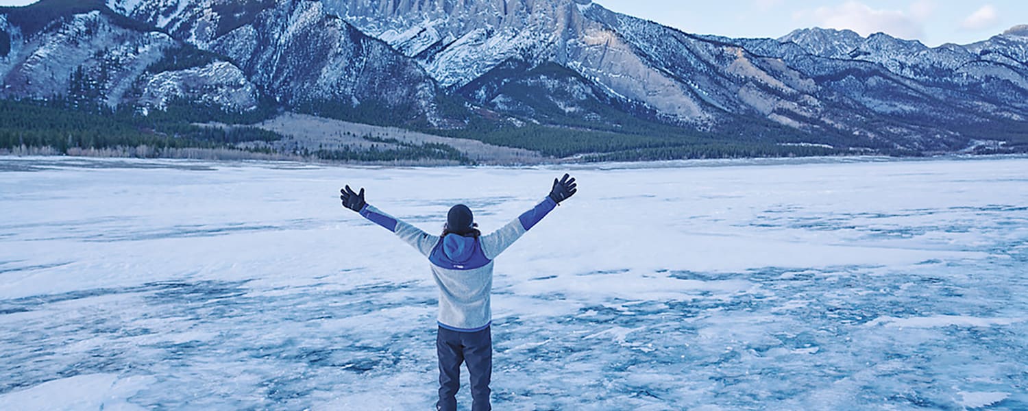 Ein Mann steht vor einem Berg im Schnee mit offenen Armen.