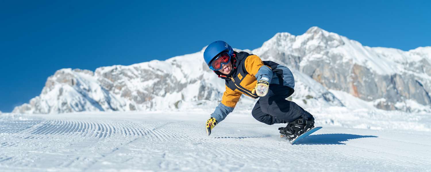 Ein Kind fährt in Snowboardbekleidung im Winter die Piste herunter.