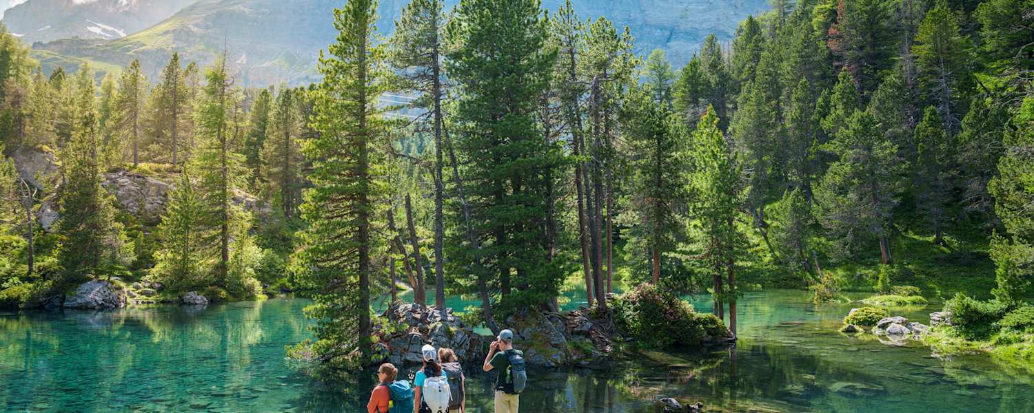 Vier Wanderer am Arvenseelo in der Schweiz, umgeben von Wasser und Wäldern.