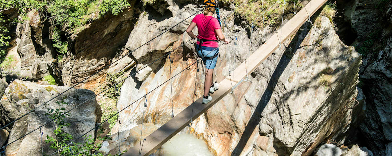 Mädchen im Klettersteigset beim Balancieren auf einem Baumstamm in der Feeschlucht