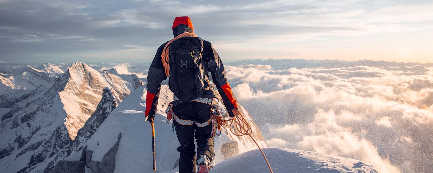 mann beim bergsteigen auf bergspitze, gekleidet in haglöfs