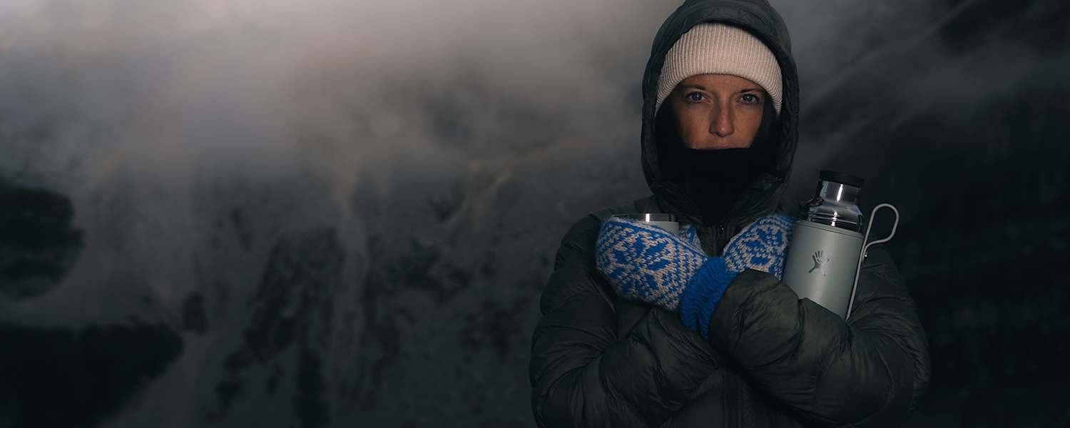 Person in Winterkleidung mit Thermosflasche Hydro Flask Hot Flask & Cup in verschneiter Berglandschaft bei Nebel und eisigen Temperaturen.
