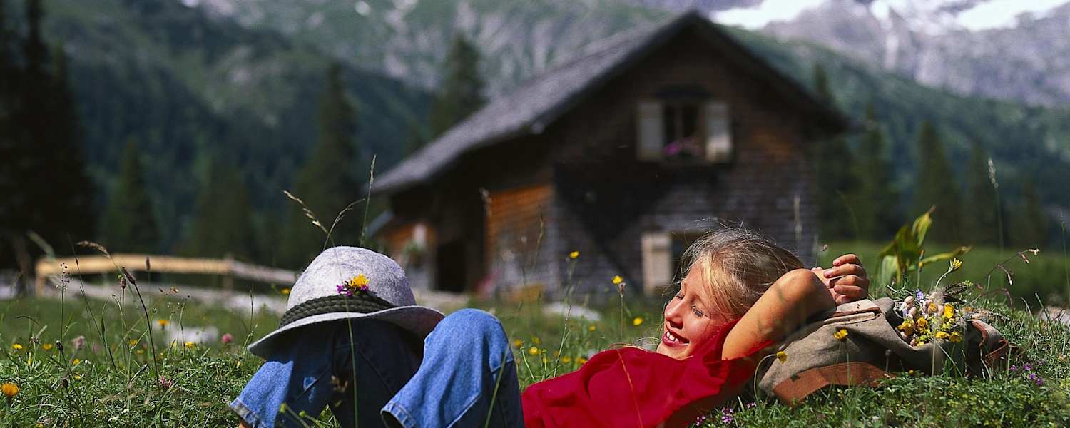 Mädchen auf einer Almwiese mit Berghütte im Hintergrund