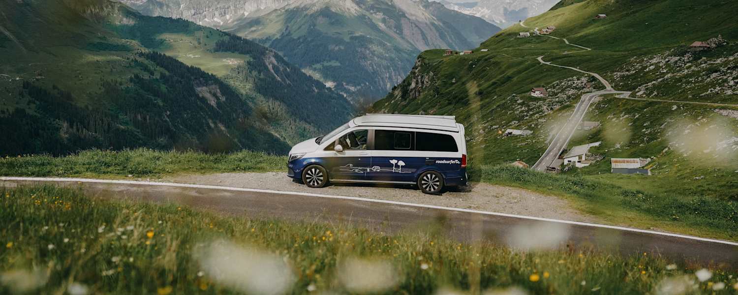 Ein Roadsurfer-Campervan steht am Straßenrand, Blick in die Berge