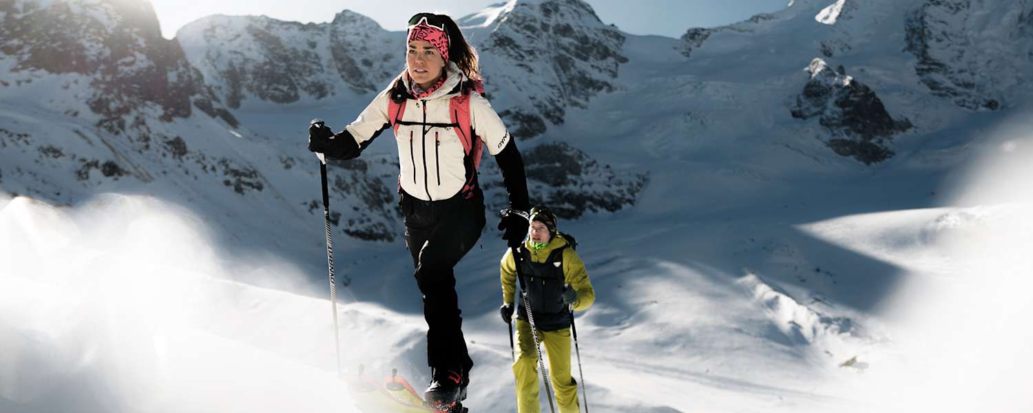 Skitourengeherin und Skitourengeher mit Dynafit-Ausrüstung beim Aufstieg im winterlichen Hochgebirge unter blauem Himmel.