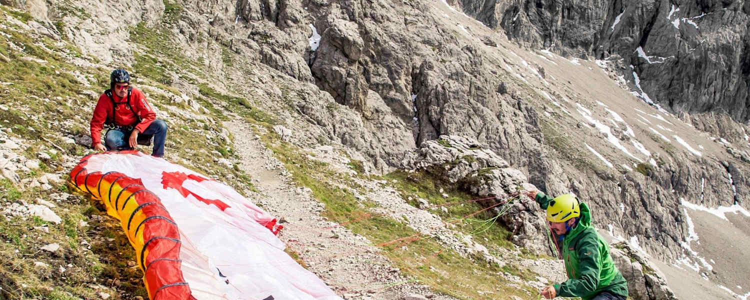 Der Tandemschirm wird vorbereitet, im Hintergrund ist eine mächtige Felswand zu sehen