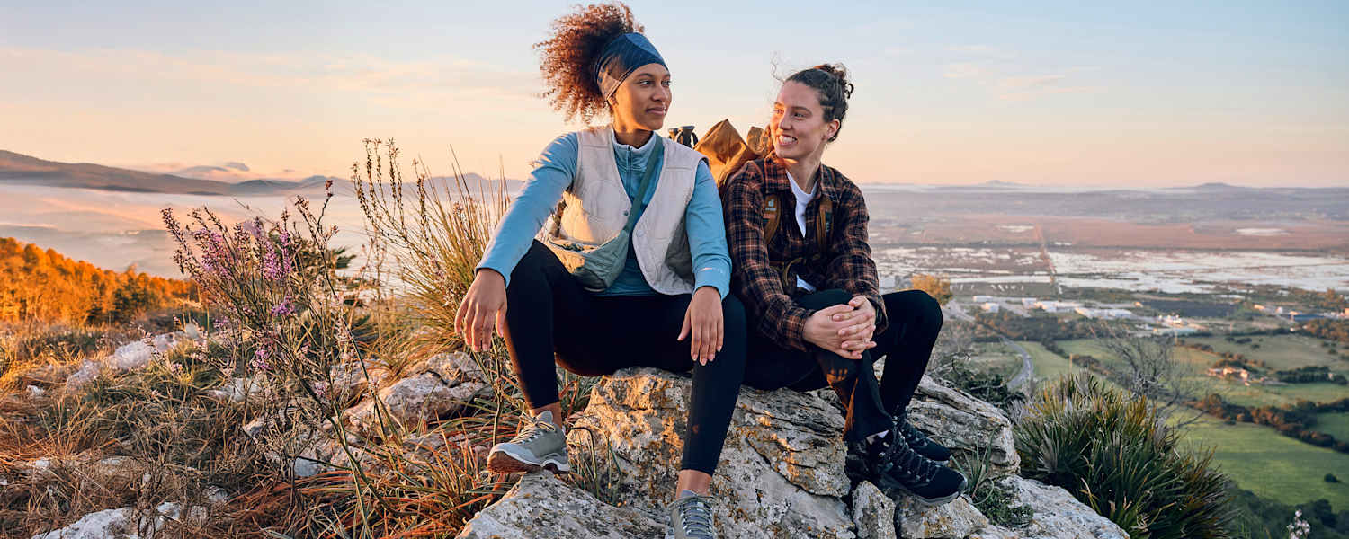 Zwei Frauen sitzen auf einem Fels in den Bergen.