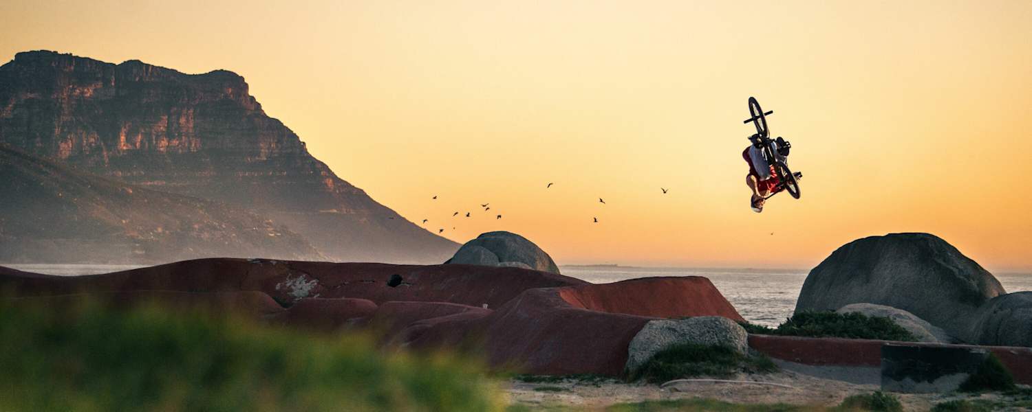 BMX-Biker dreht sich in Luft vor Küstenszenerie.