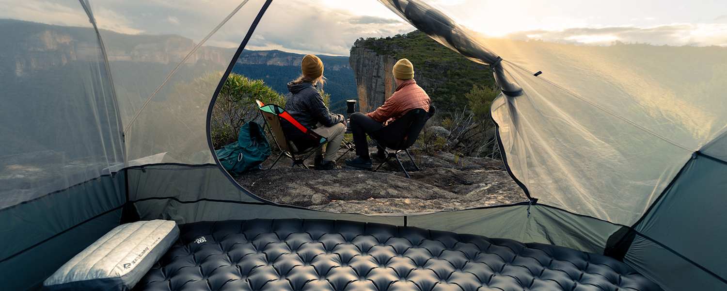 Sea to Summit Isomatte und Kissen im Zelt mit Blick auf zwei Camper, die den Sonnenuntergang in den Bergen genießen