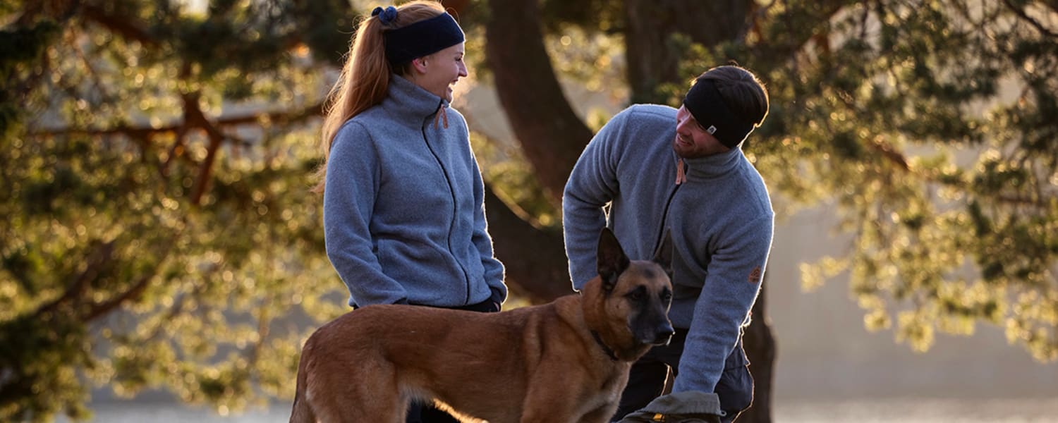 Ein Paar in Sportkleidung aus Merinowolle mit Schäferhund im Park im Herbst.