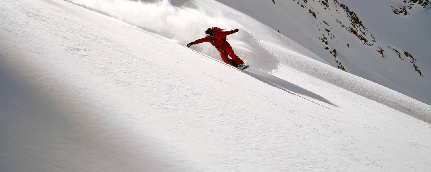 Eine Person fährt Snowboard im Schnee auf einem Berg in roter Ausrüstung.