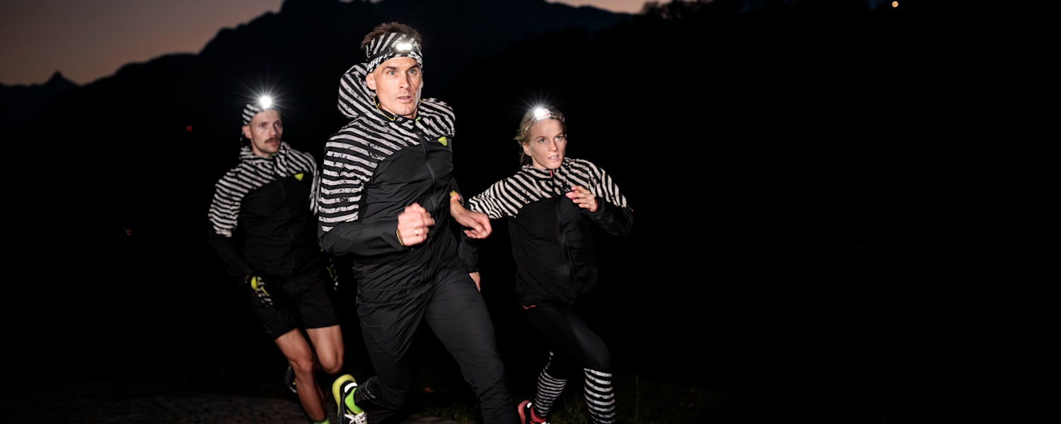 Drei Personen in reflektierender Sportkleidung in der Nacht rennend.