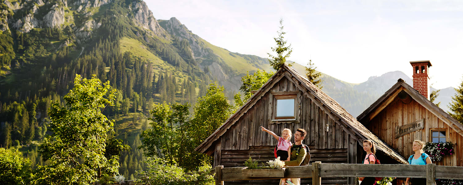 Eine Familie mit 2 Kindern steht auf einer Bergalm in der Steiermark im Sommer und beobachtet die Umgebung.