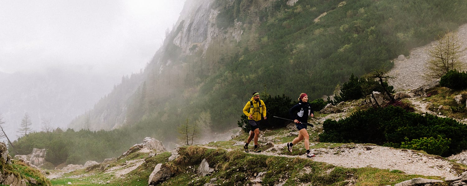 Zwei Läufer im Wald nahe eines Tals im Nebel.