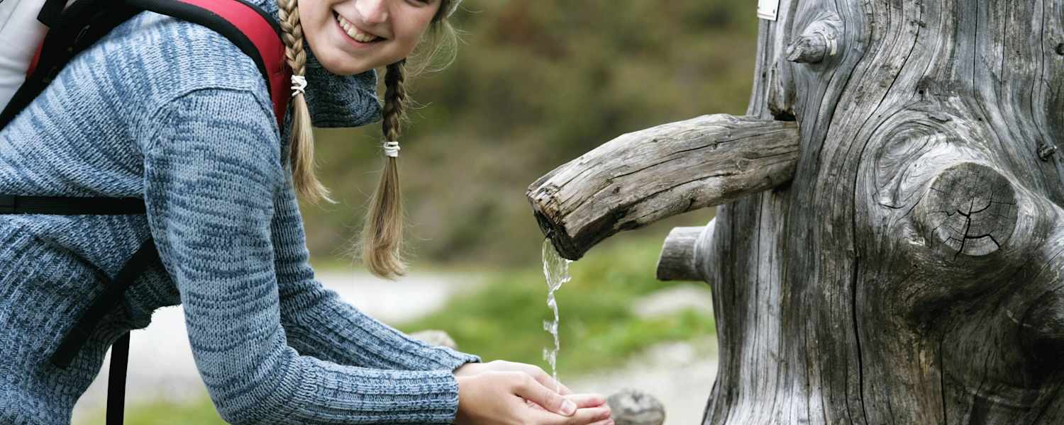 Wanderin schöpft Wasser aus einem Brunnen