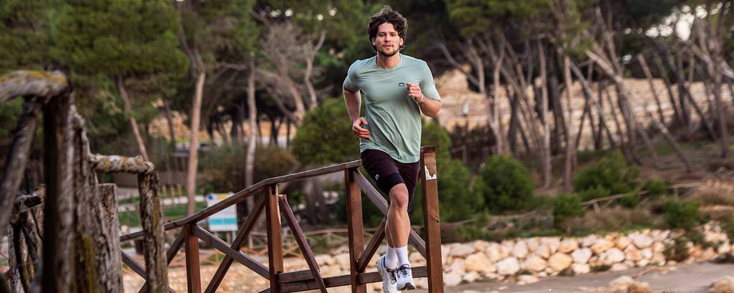 Ein Mann läuft im neuen Trailrunning-Outfit von skinfit über eine Brücke aus Holz.